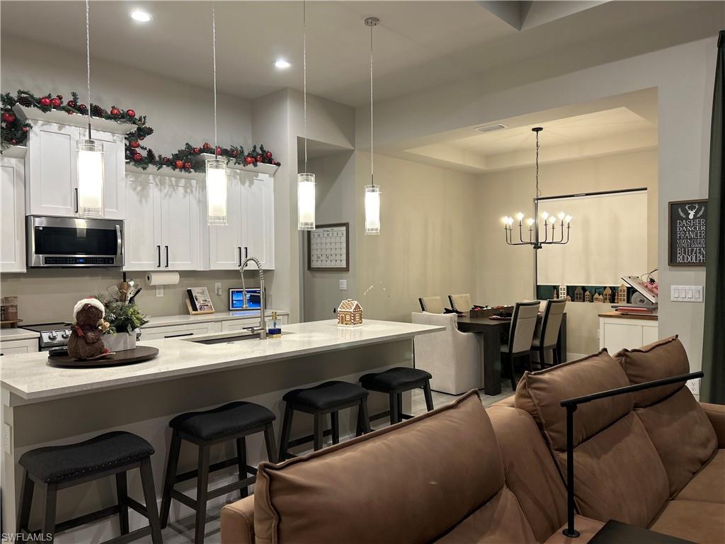 Kitchen featuring a kitchen breakfast bar, open floor plan, stainless steel microwave, white cabinetry, and a kitchen island with sink