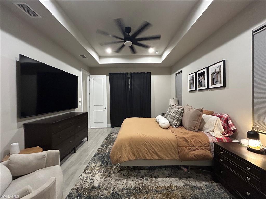 Bedroom with light wood look finished floors, a ceiling fan, and a tray ceiling