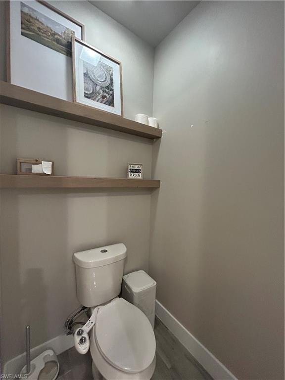 Private toilet room featuring baseboards and wood finished looking floors