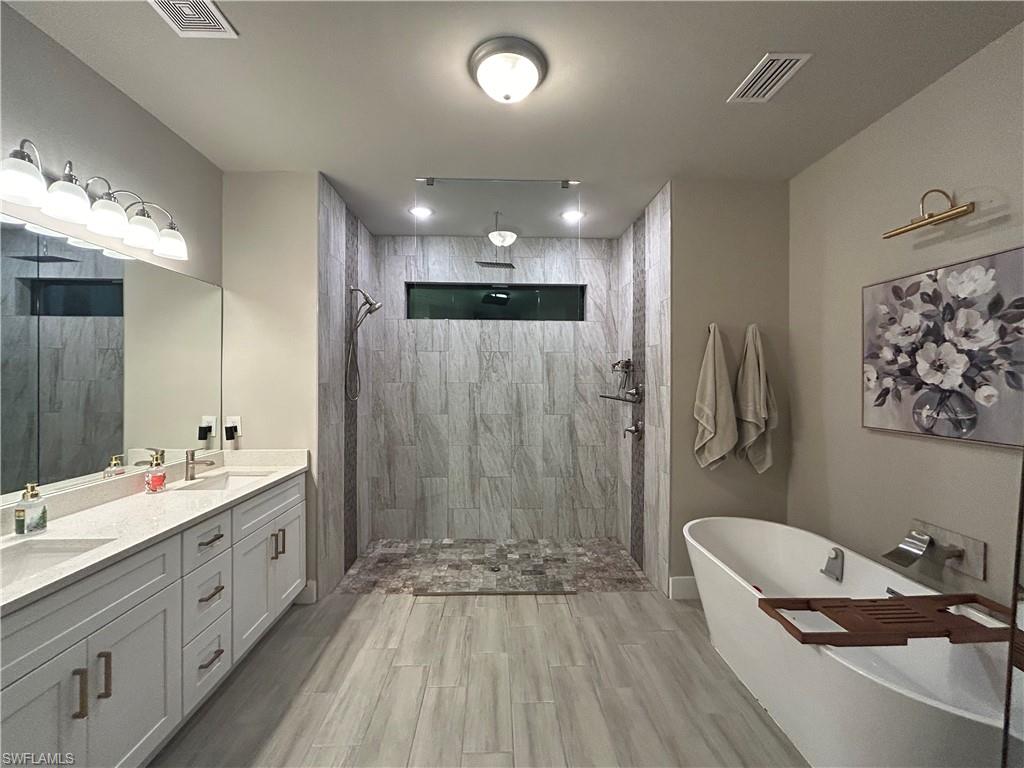 Bathroom with double vanity, walk in shower, a soaking tub, and wood looking finish floors
