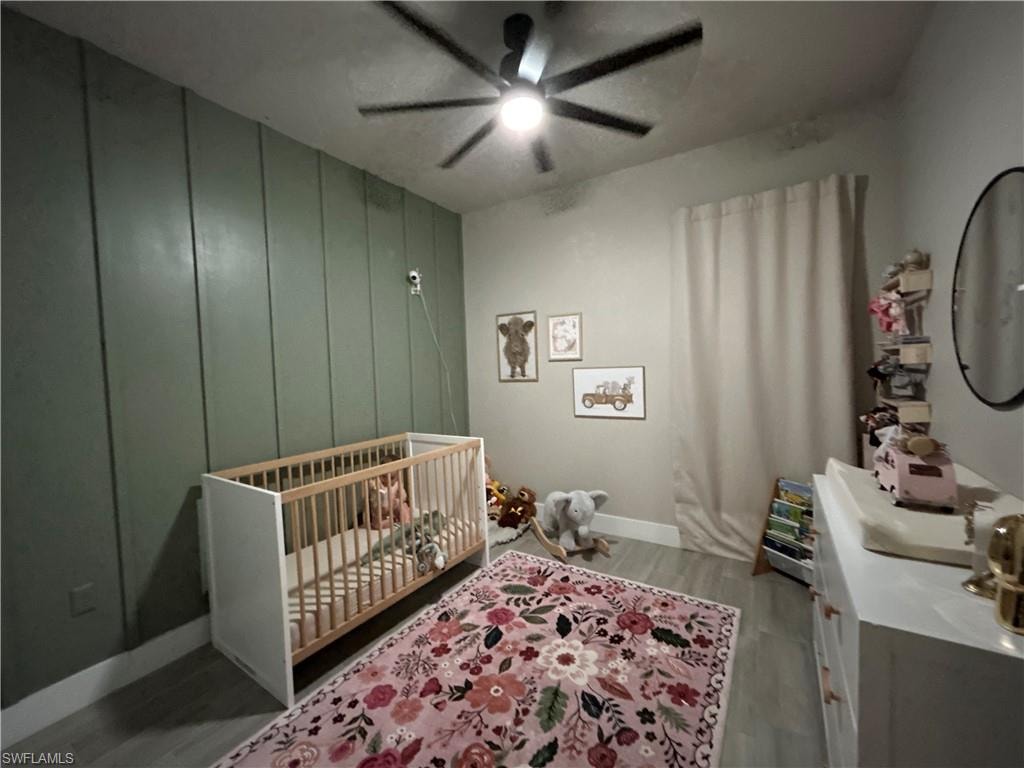 Bedroom featuring a nursery area, light wood look flooring, and a ceiling fan