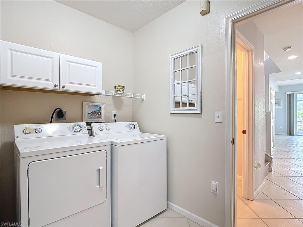 Laundry area with light tile patterned floors, independent washer and dryer, and cabinet space