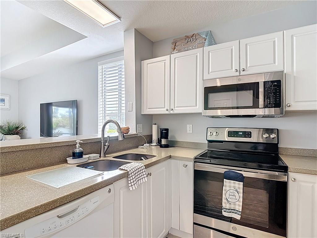 Kitchen with stainless steel appliances, white cabinets, a textured ceiling, and light stone countertops