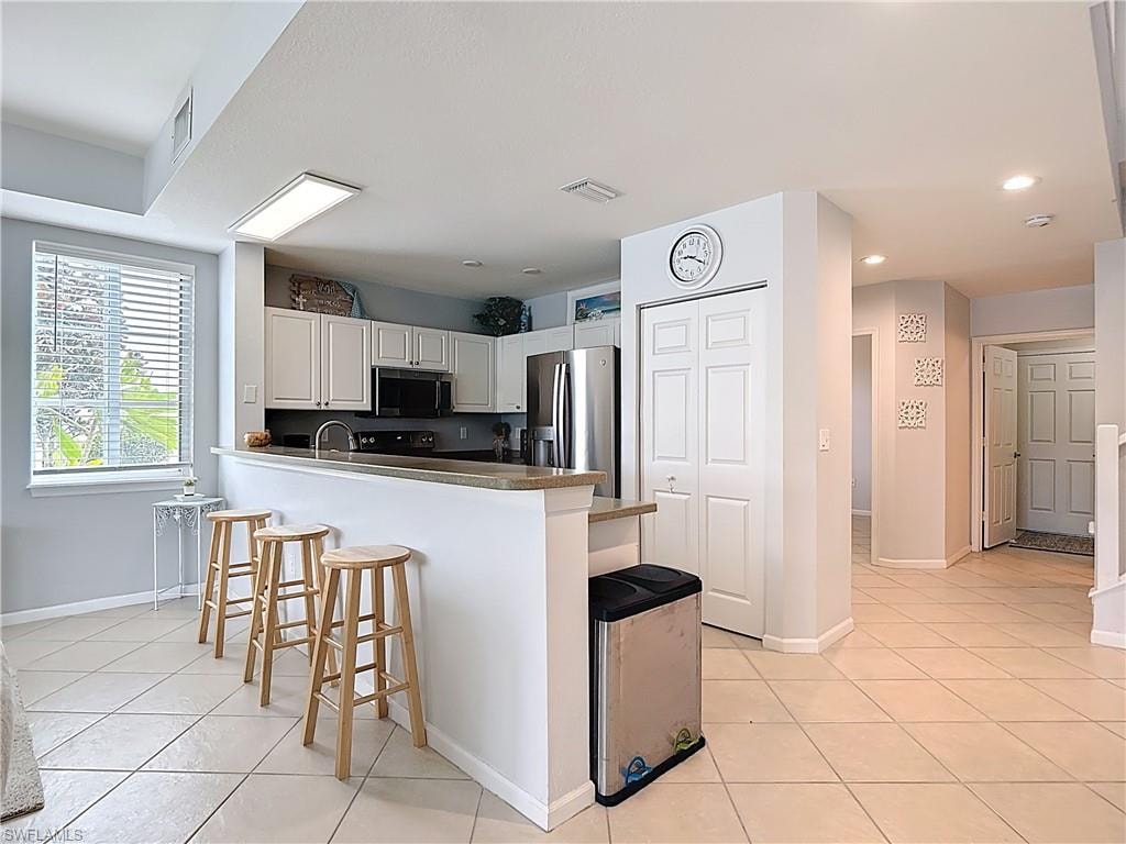 Kitchen with white cabinets, appliances with stainless steel finishes, a breakfast bar, light tile patterned flooring, and a peninsula
