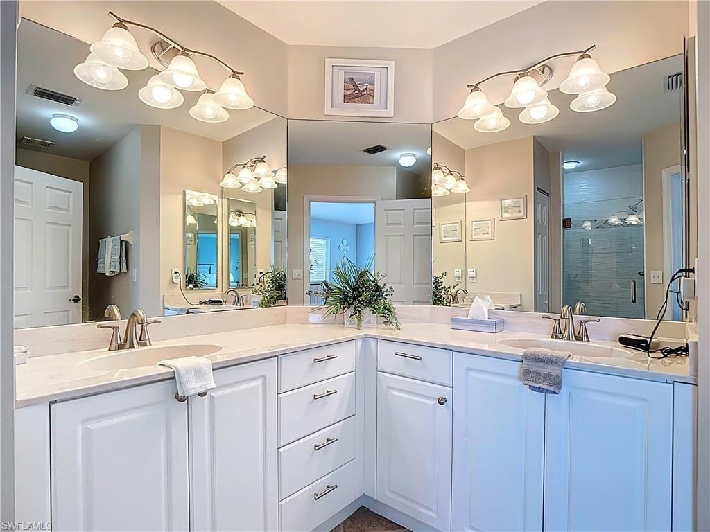 Full bath featuring double vanity, a stall shower, and a chandelier