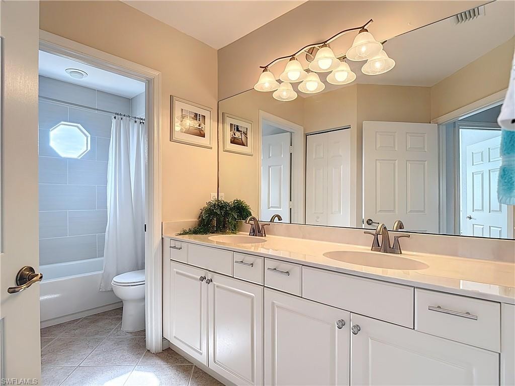 Bathroom with double vanity, shower / tub combo, and light tile patterned floors