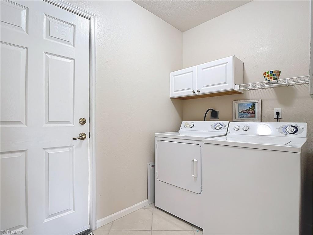 Laundry room featuring light tile patterned floors, independent washer and dryer, a textured ceiling, and cabinet space