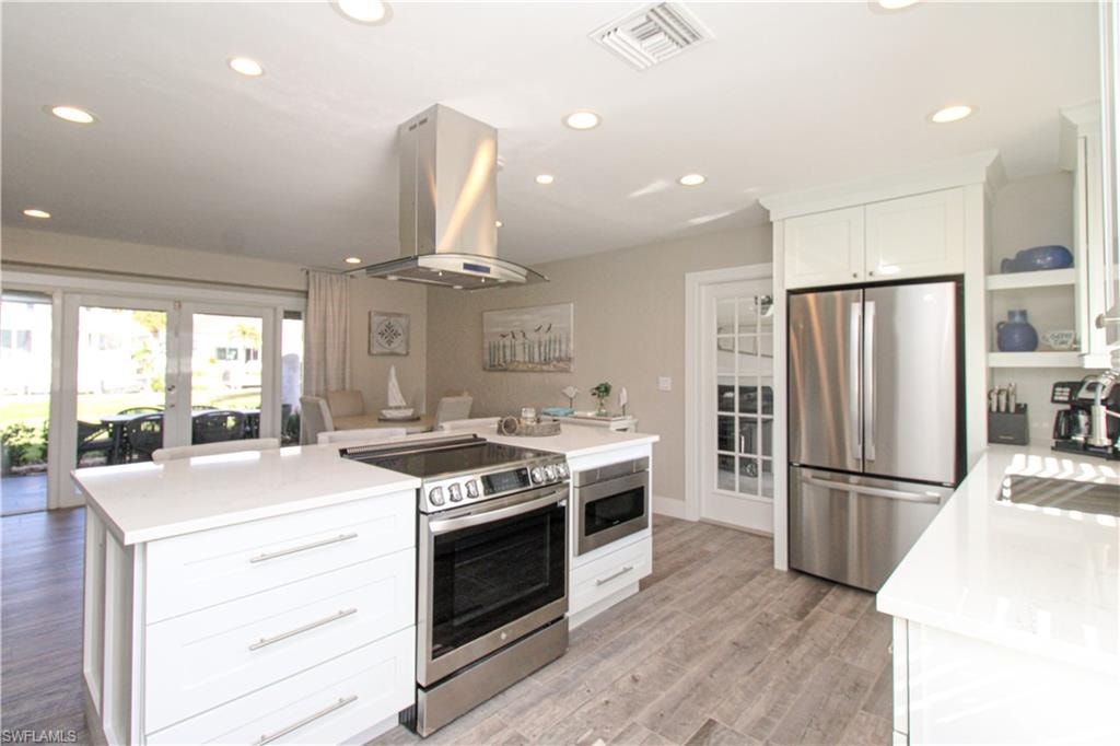 Kitchen featuring white cabinetry, sink, stainless steel appliances, light hardwood / wood-style flooring, and island exhaust hood