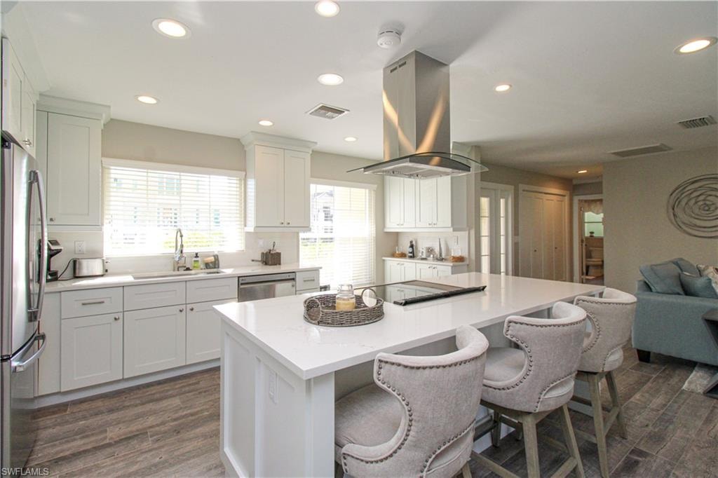 Kitchen featuring island exhaust hood, appliances with stainless steel finishes, a kitchen island, sink, and white cabinetry
