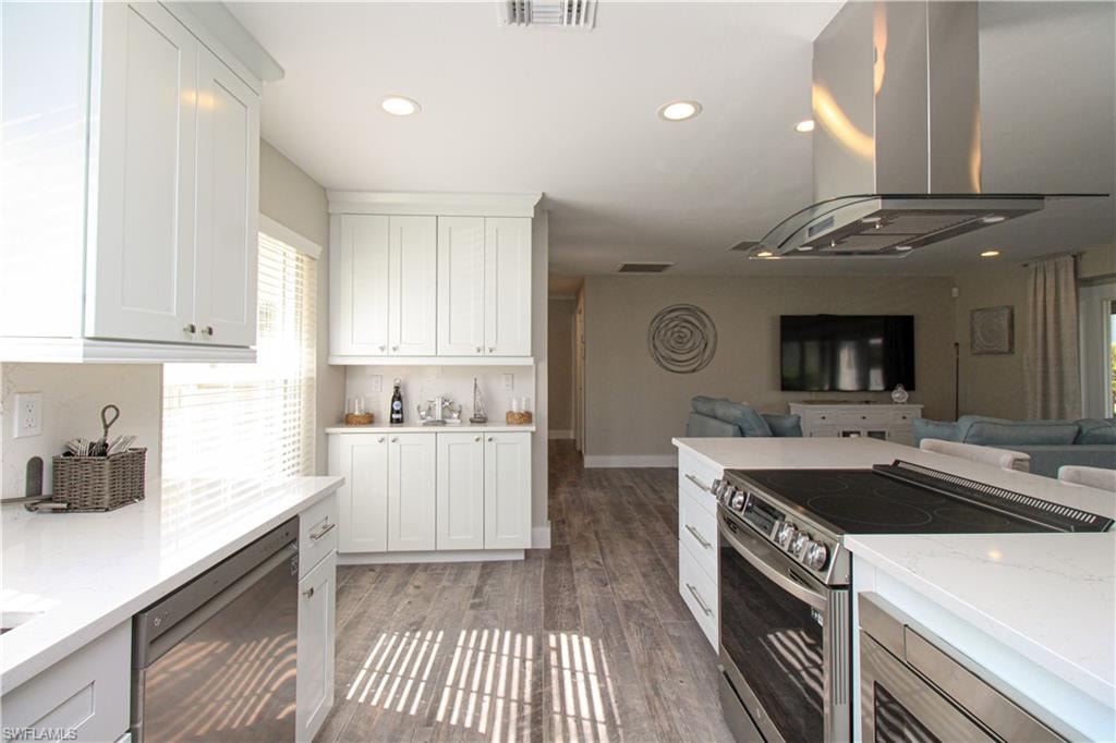 Kitchen featuring white cabinetry, island range hood, dark wood-type flooring, and stainless steel appliances