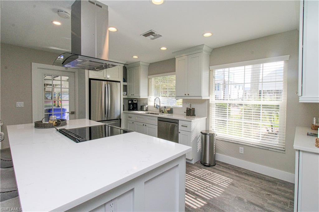 Kitchen featuring white cabinets, sink, appliances with stainless steel finishes, island range hood, and wood-type flooring