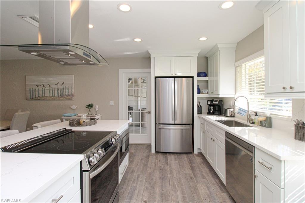 Kitchen with sink, stainless steel appliances, island exhaust hood, light hardwood / wood-style floors, and white cabinets