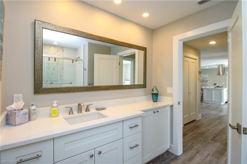 Bathroom with vanity, a shower with shower door, and wood-type flooring
