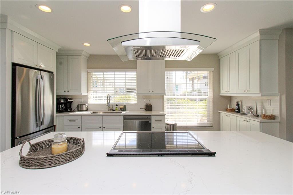 Kitchen with white cabinets, appliances with stainless steel finishes, island range hood, and sink