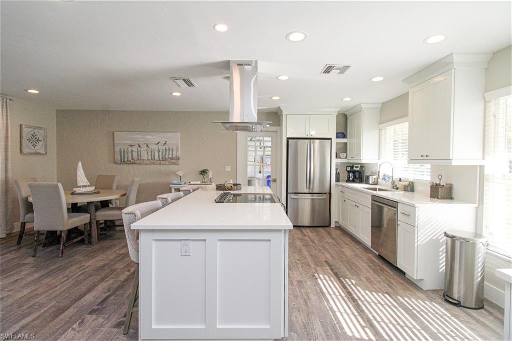 Kitchen with sink, stainless steel appliances, a kitchen island, island exhaust hood, and white cabinets
