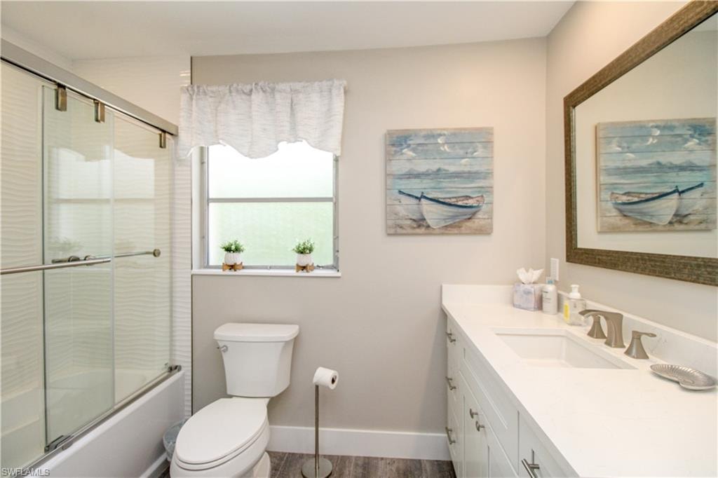 Full bathroom with hardwood / wood-style flooring, vanity, toilet, and enclosed tub / shower combo