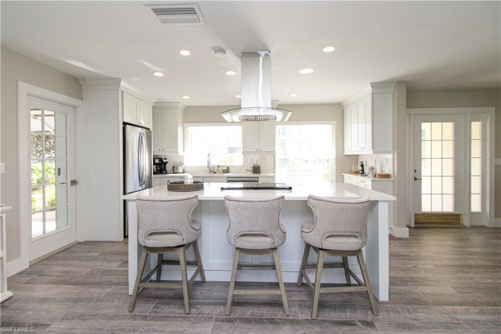 Kitchen with white cabinets, a kitchen island, island exhaust hood, and a wealth of natural light