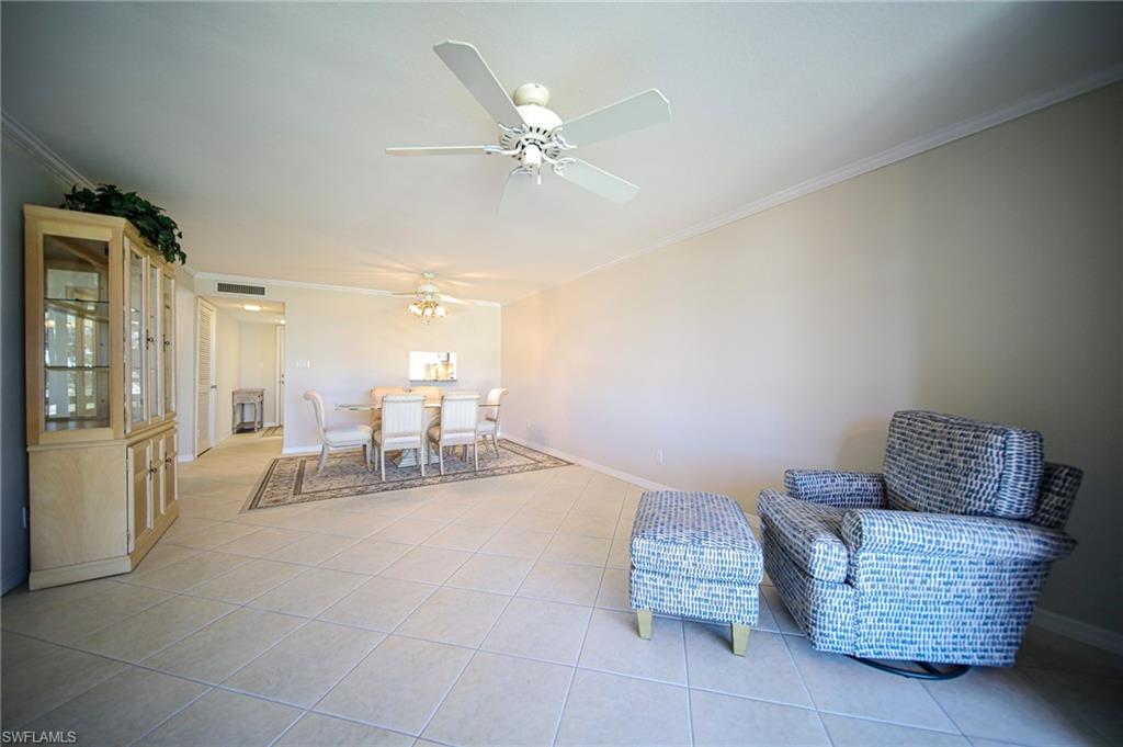 There Is A Large Living Room With Crown Molding, Ceiling Fan, Chair With Ottoman, And Wooden & Glass Cabinet!