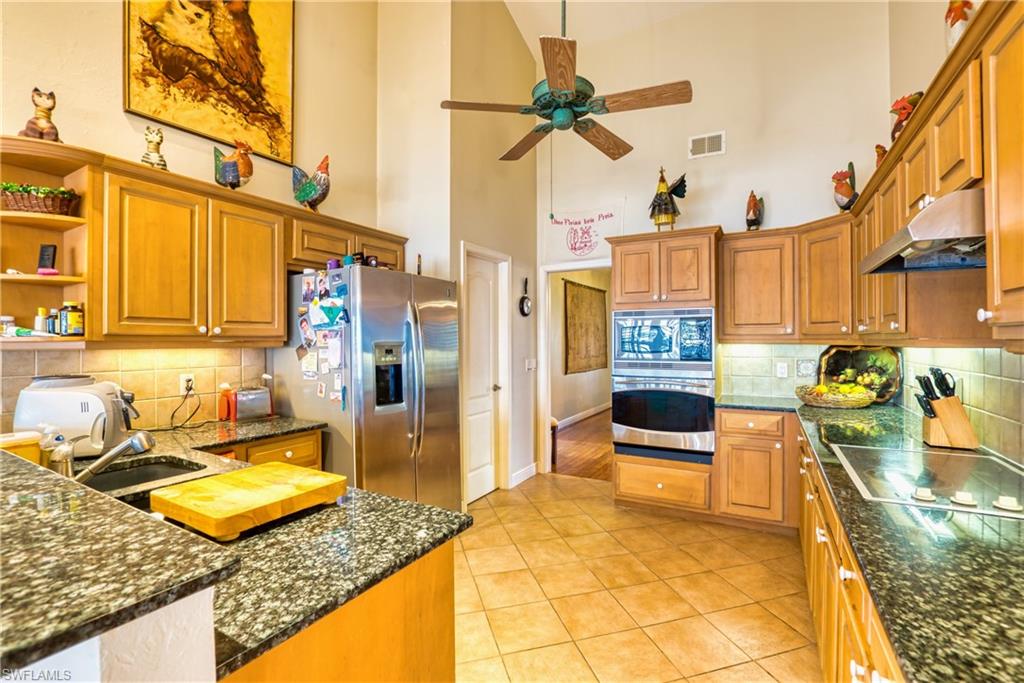 Kitchen featuring decorative backsplash, brown cabinetry, a high ceiling, stainless steel appliances, and under cabinet range hood