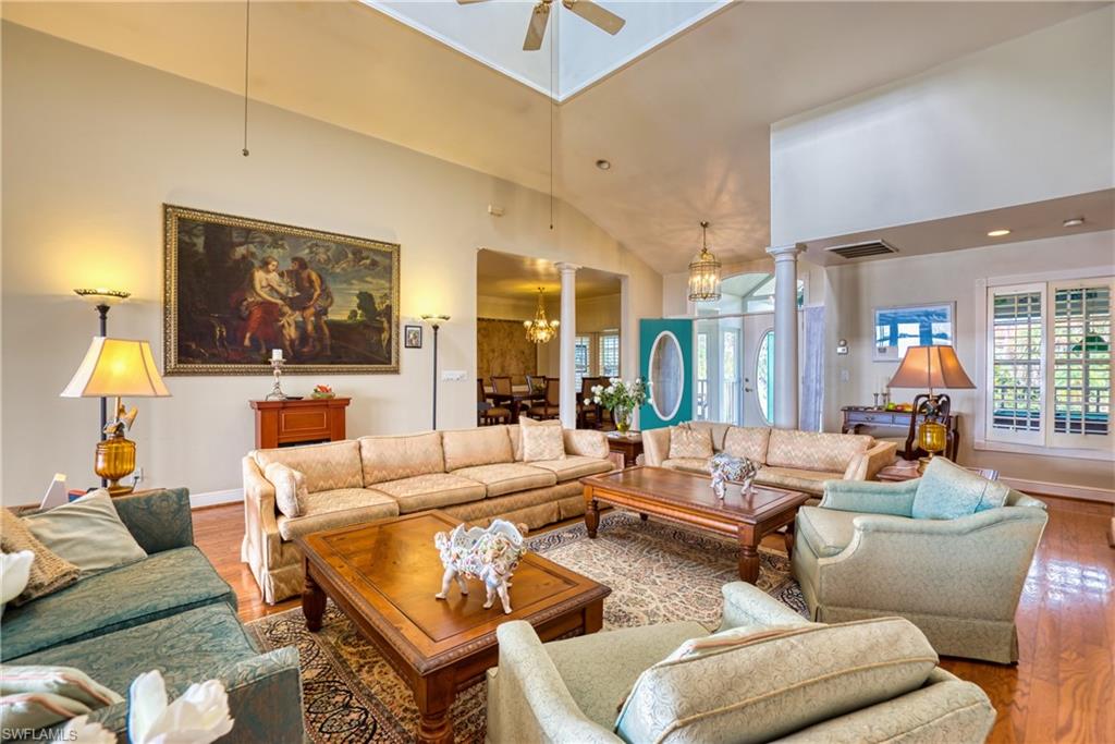 Living room with a chandelier, ornate columns, lofted ceiling, wood finished floors, and a ceiling fan