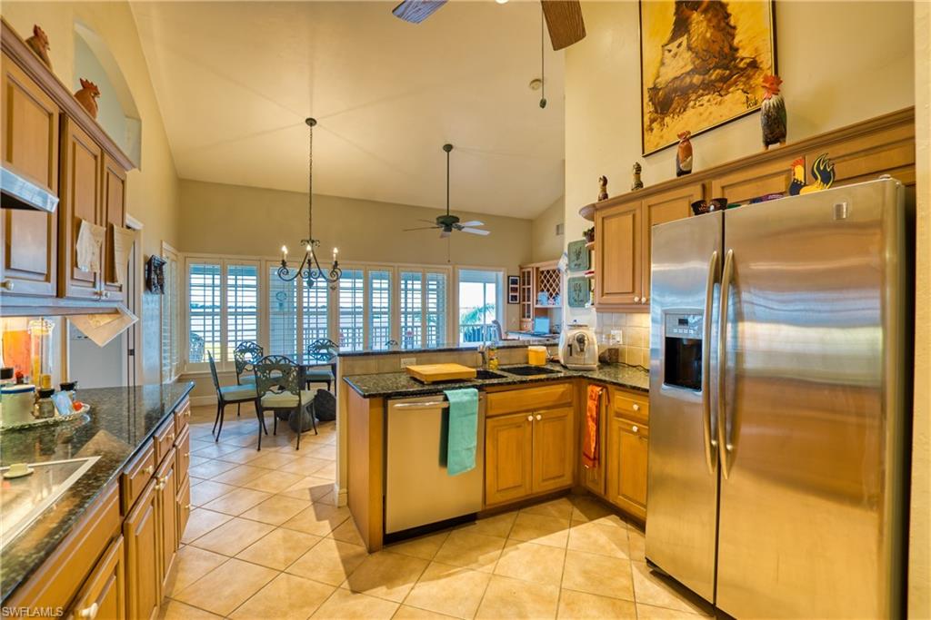 Kitchen with stainless steel refrigerator with ice dispenser, brown cabinetry, dark stone counters, ceiling fan, and high vaulted ceiling