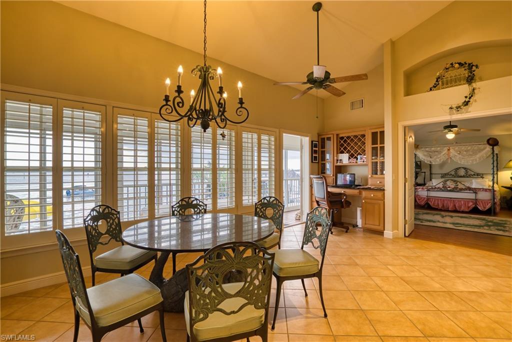 Dining space with built in study area, light tile patterned flooring, high vaulted ceiling, a chandelier, and a ceiling fan
