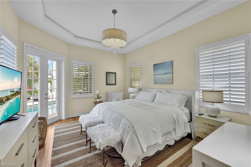 Bedroom with wood-type flooring, a tray ceiling, access to outside, and french doors