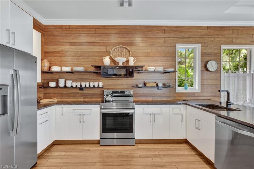 Kitchen with appliances with stainless steel finishes, white cabinetry, dark stone counters, and sink