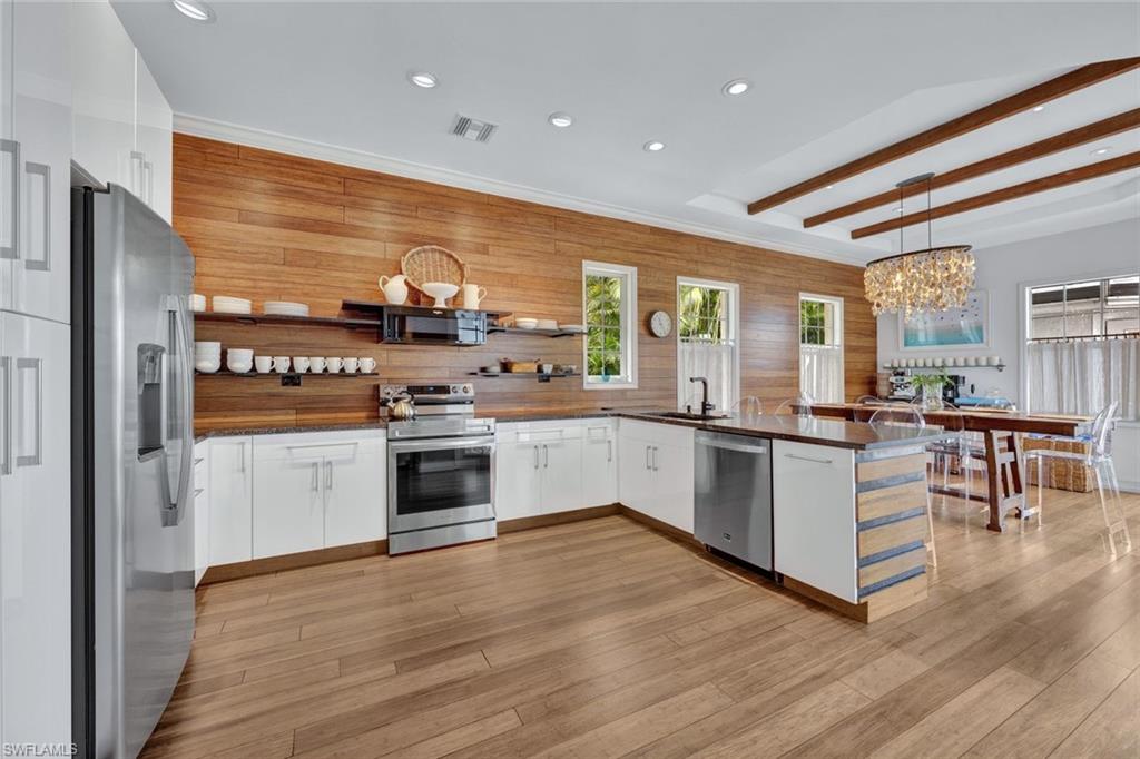 Kitchen featuring pendant lighting, kitchen peninsula, an inviting chandelier, appliances with stainless steel finishes, and white cabinets