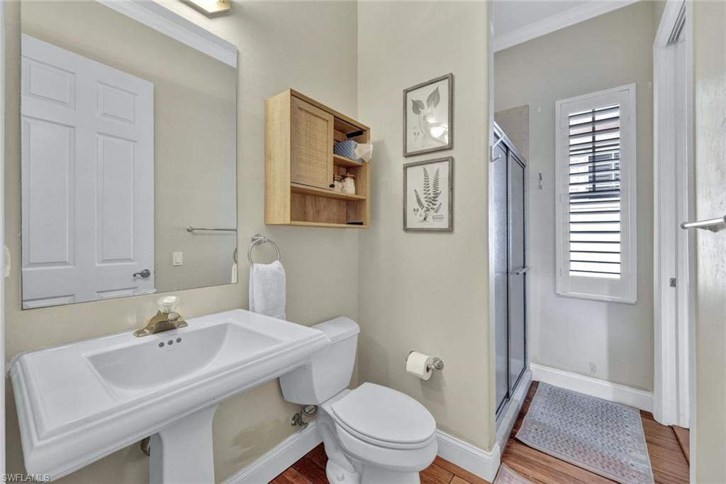 Bathroom with toilet, hardwood / wood-style floors, walk in shower, crown molding, and sink