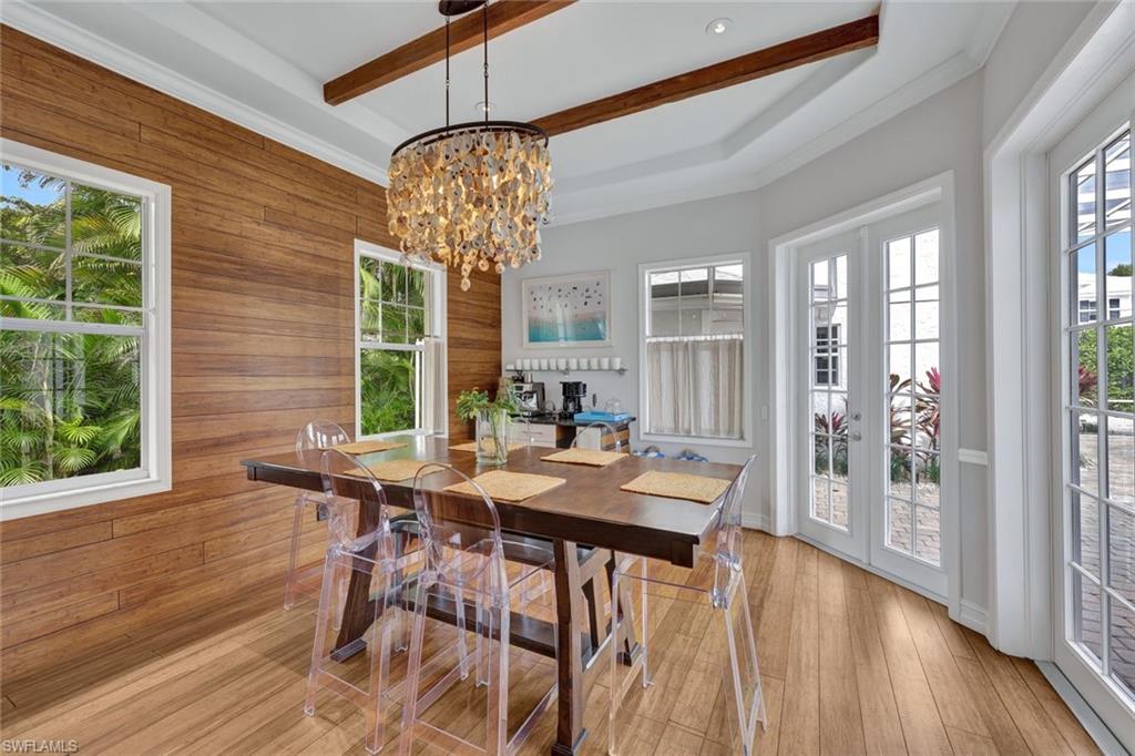 Dining room with french doors, beamed ceiling, wood walls, and a chandelier