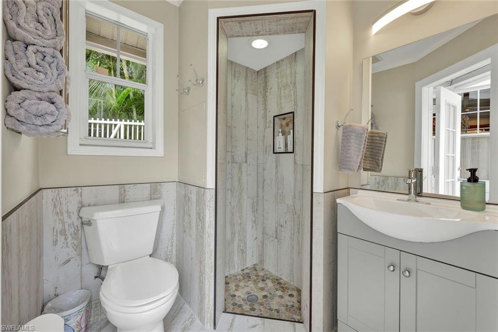 Bathroom featuring tile walls, tiled shower, vanity, and toilet