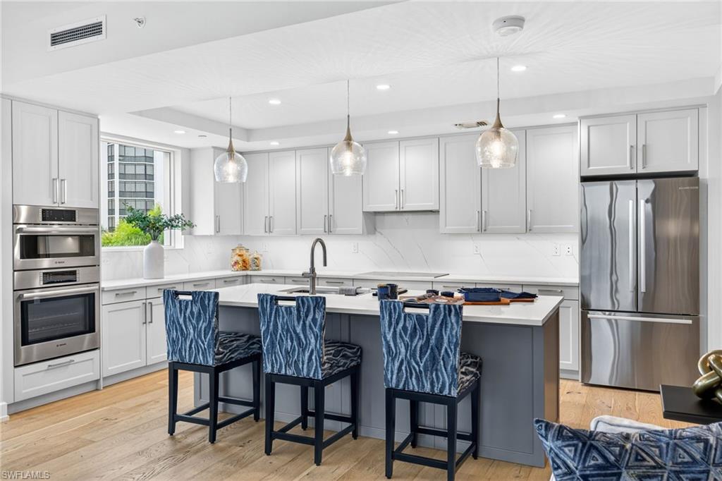 Stunning kitchen with stainless steel appliances, hanging light fixtures, a kitchen bar, a kitchen island with sink, and recessed lighting