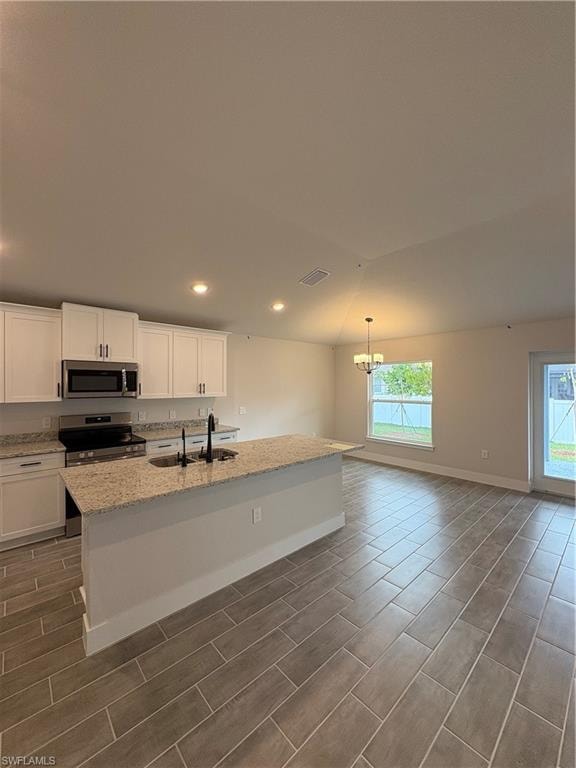 Kitchen with vaulted ceiling, a center island with sink, white cabinets, light stone counters, and recessed lighting