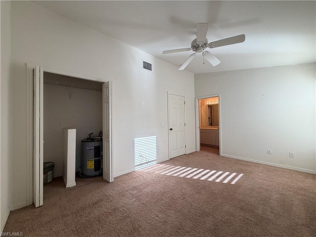 Unfurnished bedroom featuring vaulted ceiling, electric water heater, ensuite bathroom, ceiling fan, and a closet