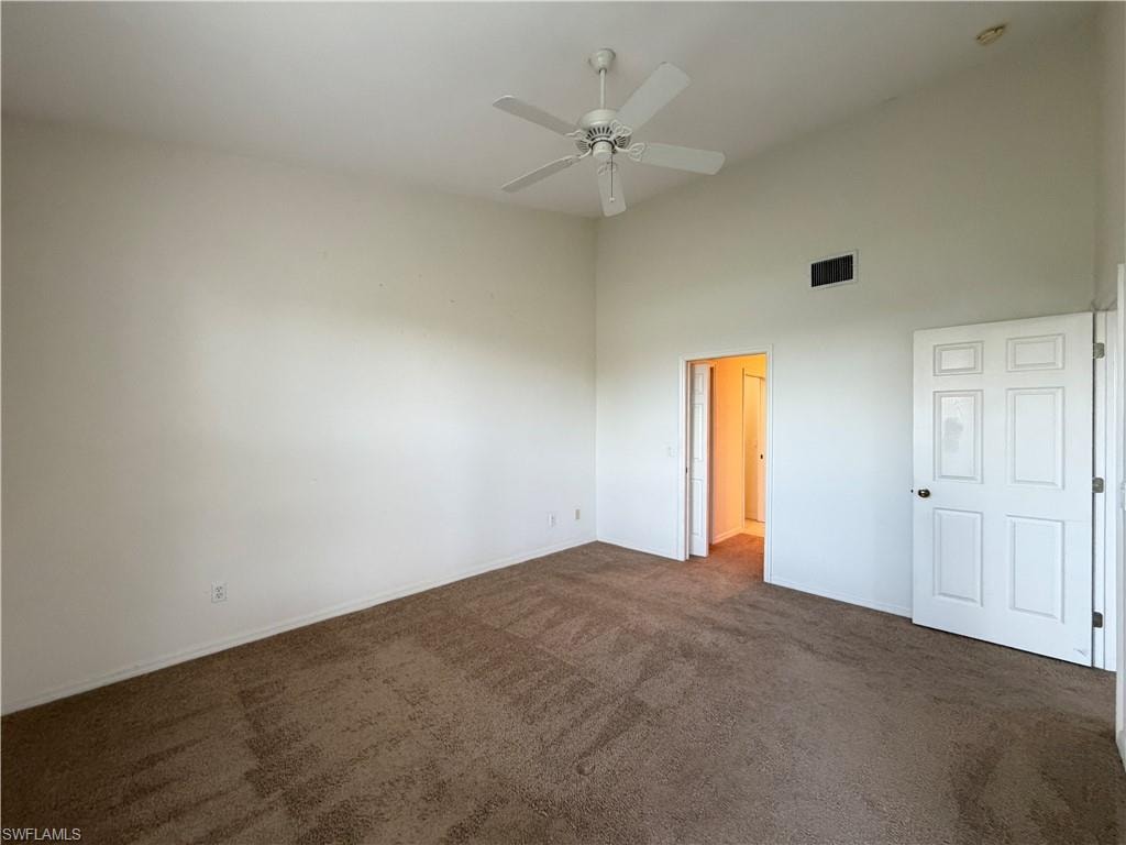Unfurnished bedroom featuring dark carpet, ceiling fan, and a towering ceiling