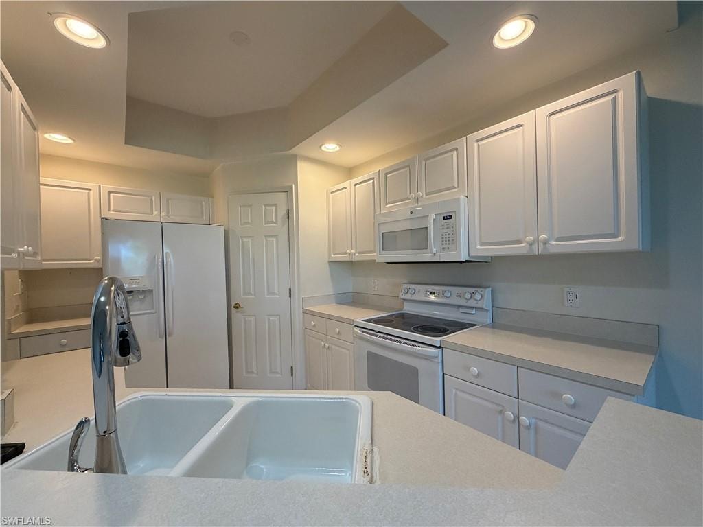 Kitchen with light countertops, white appliances, white cabinetry, recessed lighting, and a tray ceiling