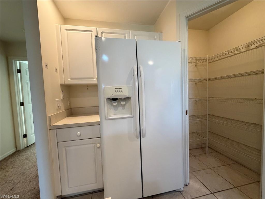 Kitchen featuring white refrigerator with ice dispenser, white cabinetry, and light countertops