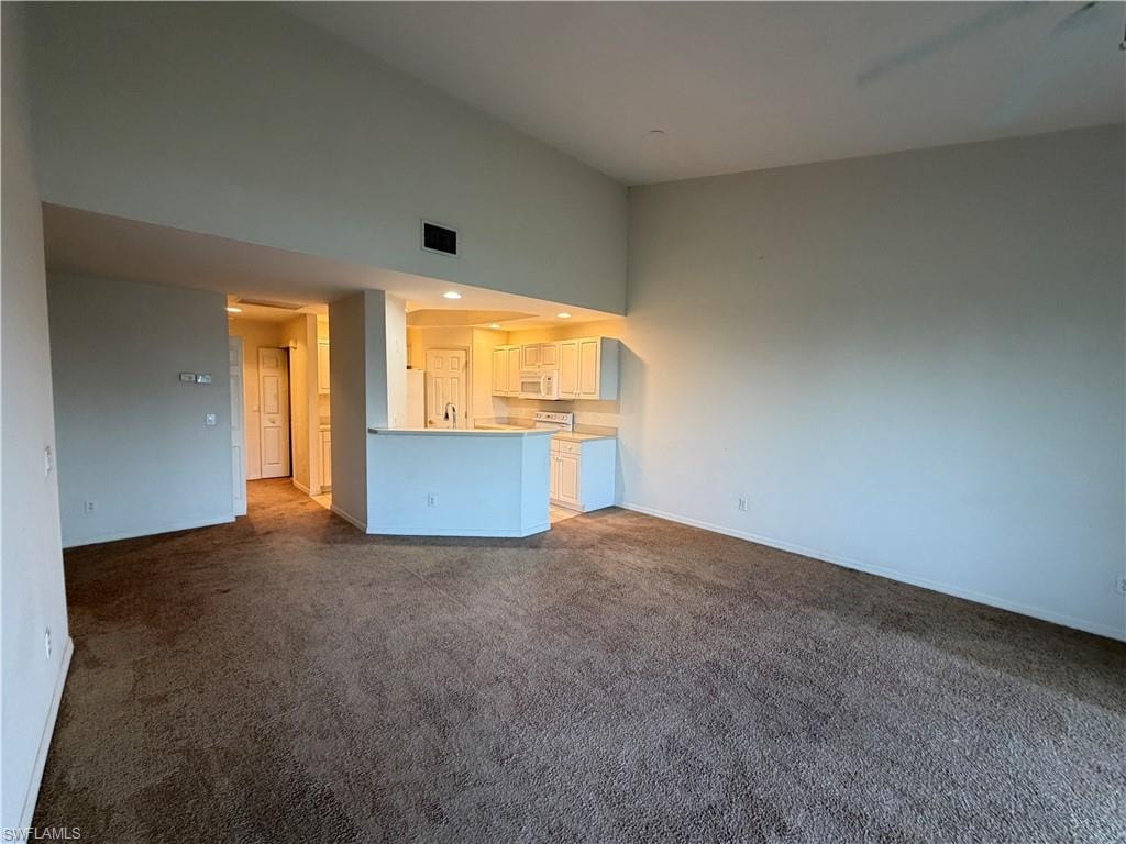 Unfurnished living room featuring a high ceiling, dark carpet, and recessed lighting
