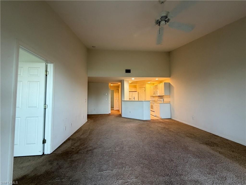 Unfurnished living room featuring ceiling fan, dark colored carpet, and a high ceiling
