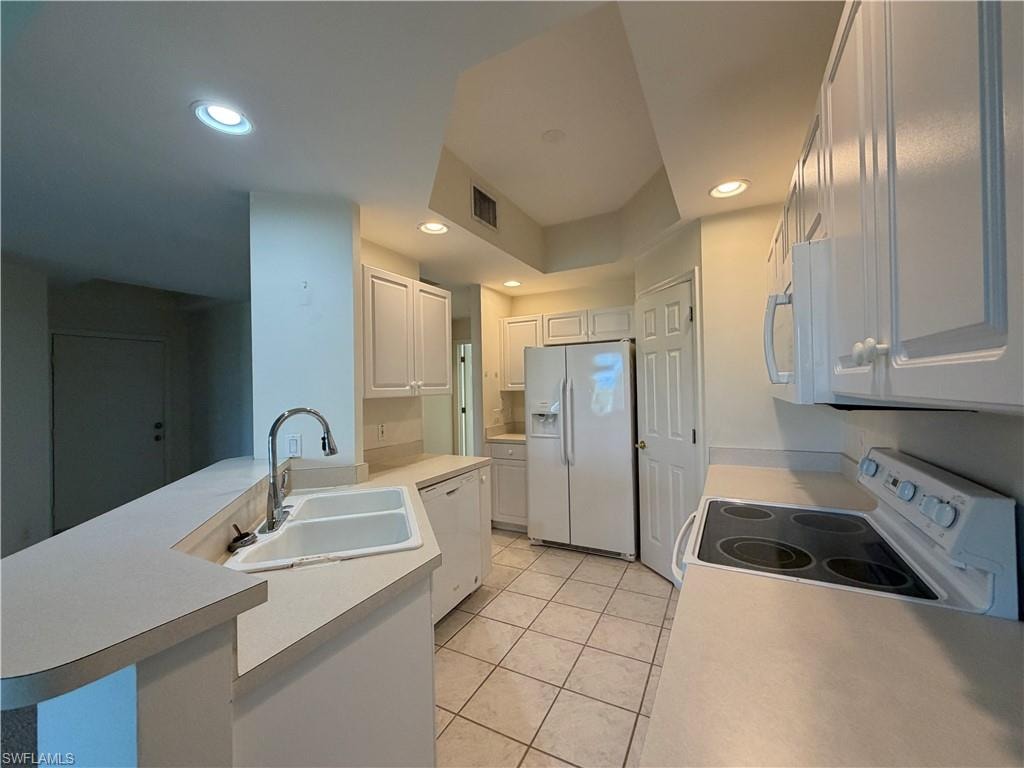 Kitchen featuring a peninsula, white appliances, light countertops, white cabinetry, and recessed lighting