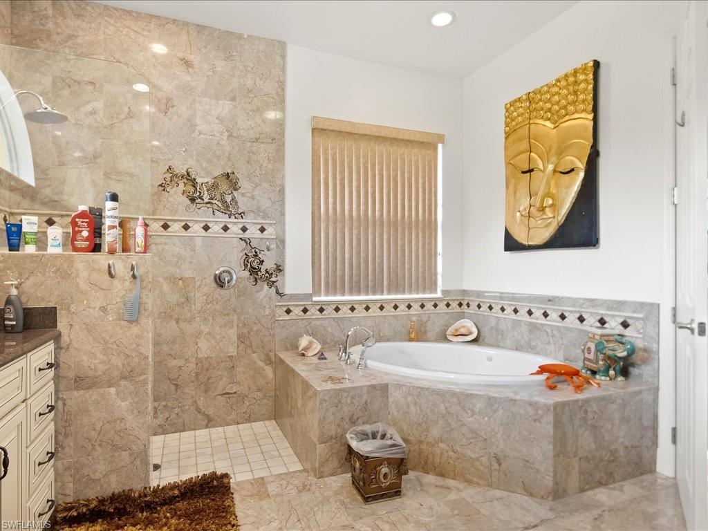 Full bath featuring walk in shower, a garden tub, vanity, and marble finish floors