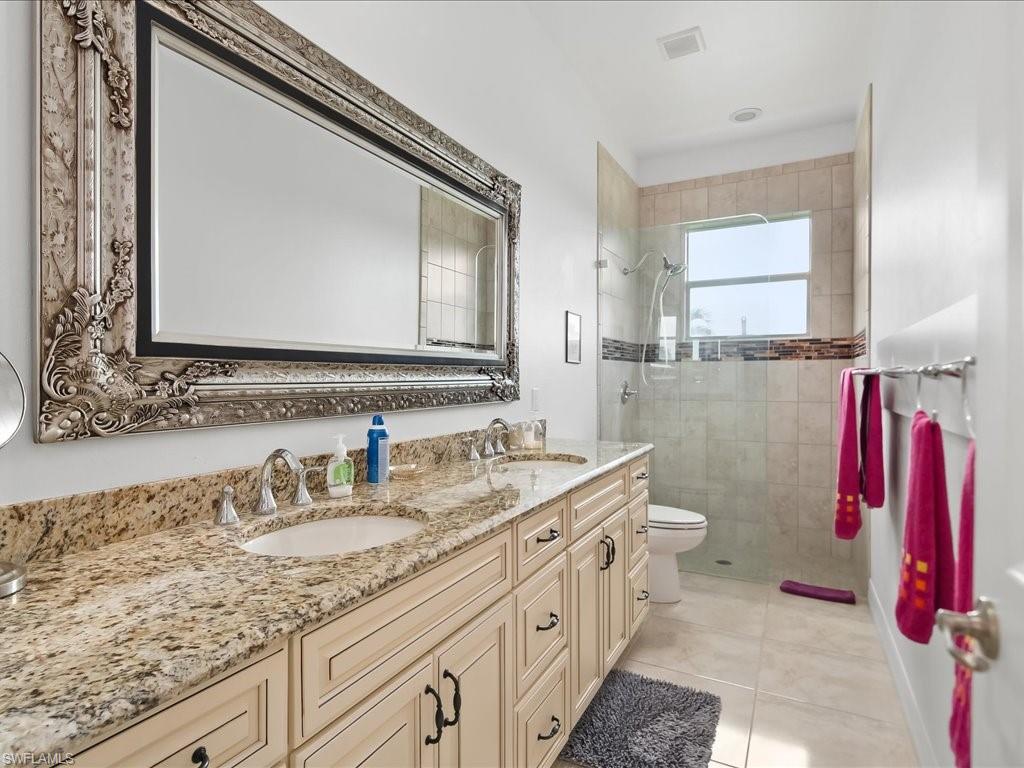 Bathroom with double vanity, a tile shower, and light tile patterned floors