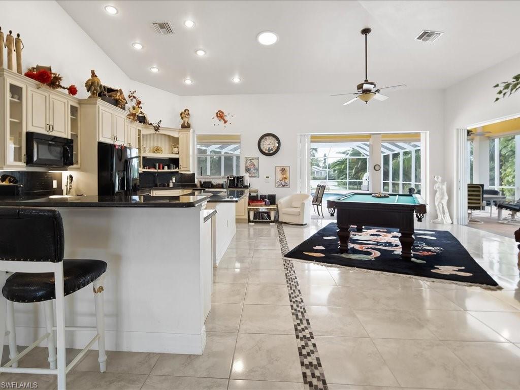 Kitchen featuring billiards, a breakfast bar area, black appliances, glass insert cabinets, and healthy amount of natural light