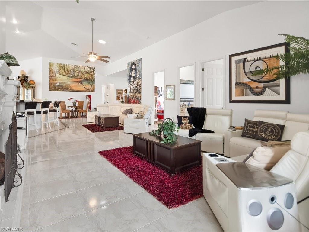 Living area featuring lofted ceiling, ceiling fan, light marble finish floors, and recessed lighting