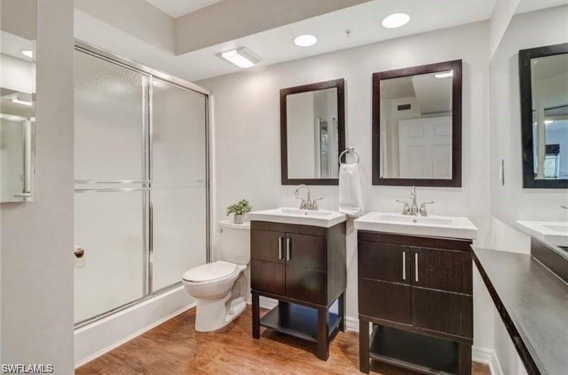 Bathroom with two vanities, a stall shower, light wood-style floors, and recessed lighting