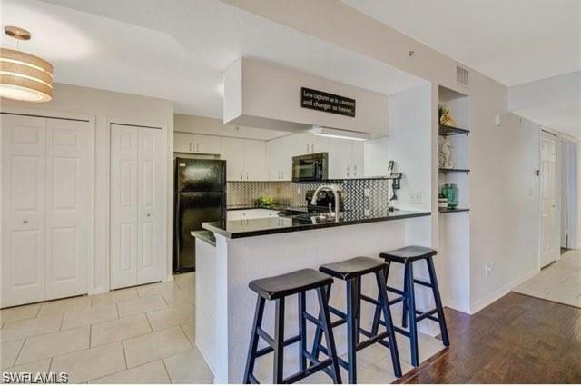 Kitchen featuring a breakfast bar area, black appliances, dark countertops, a peninsula, and backsplash