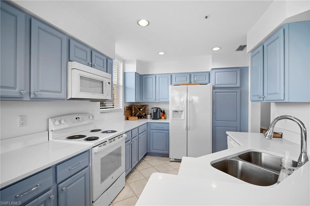 Kitchen featuring white appliances, recessed lighting, blue cabinets, light tile patterned floors, and light stone counters