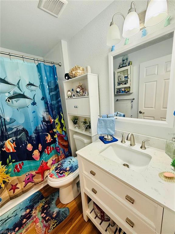 Full bath with a textured wall, vanity, wood finished floors, a shower with shower curtain, and a textured ceiling