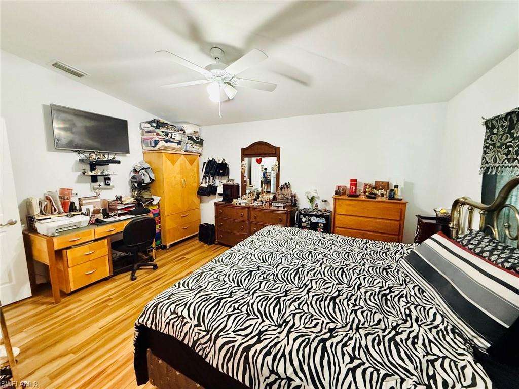 Bedroom with light wood-type flooring, an office area, and a ceiling fan
